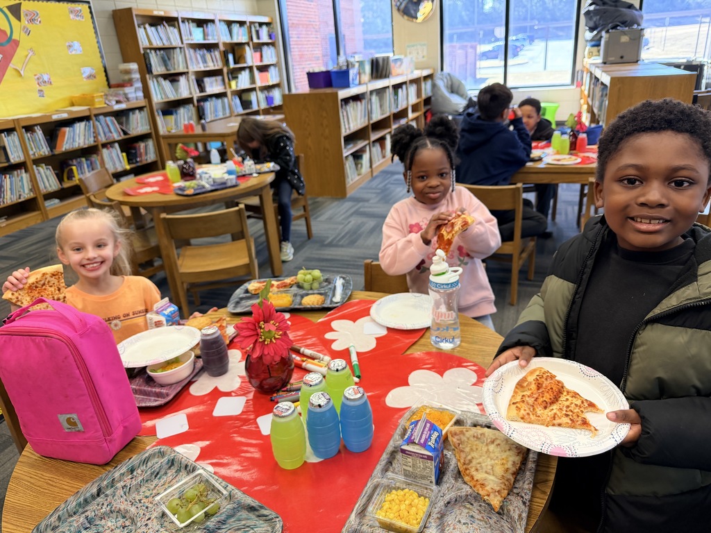 Kids smiling for a picture and eating pizza at the pizza party. 