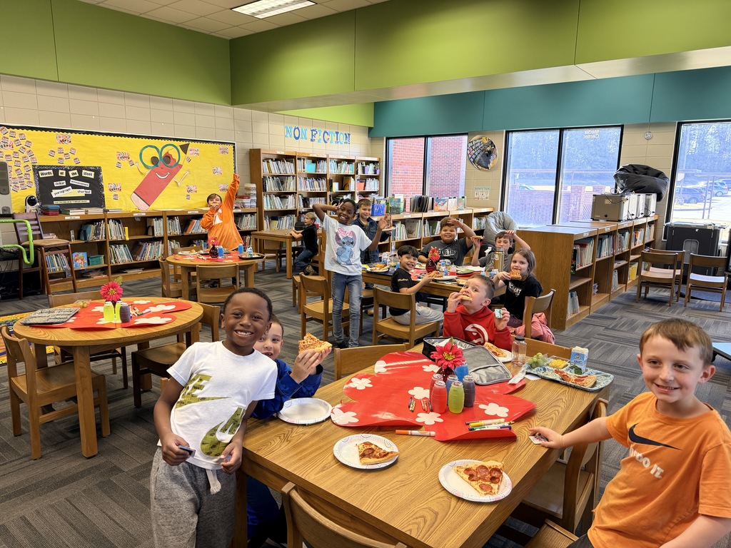 Kids smiling for a picture and eating pizza at the pizza party. 