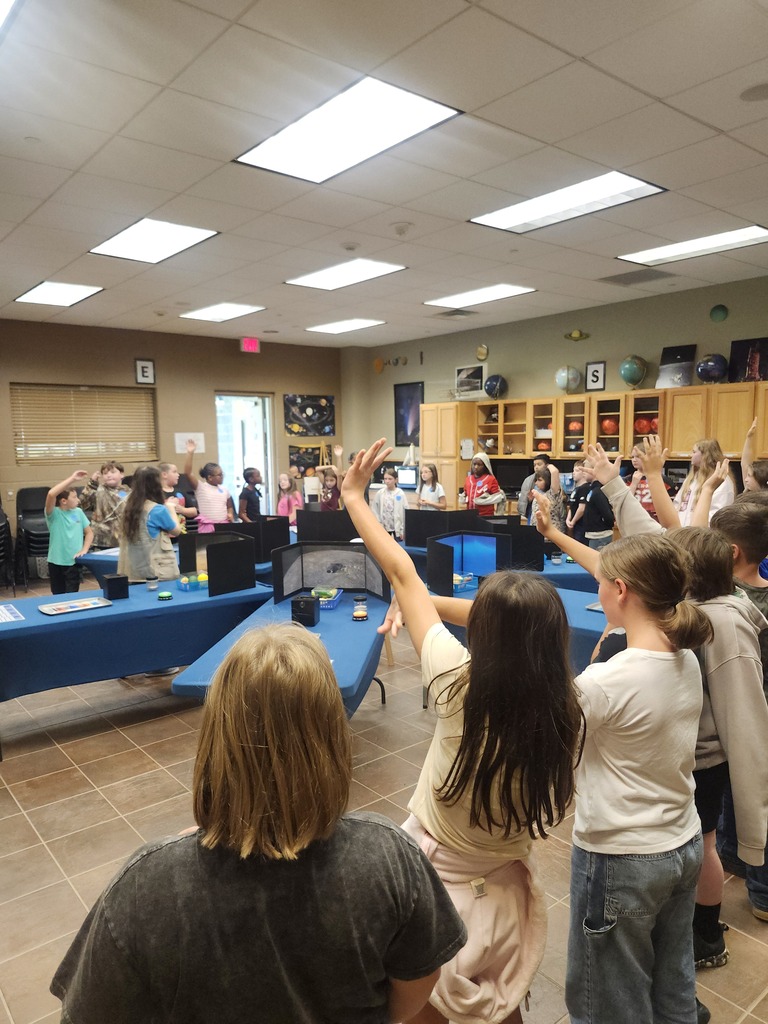 Picture of 4th grade students learning hands on activities on a field trip. Large whole class picture of kids with hands raised. 