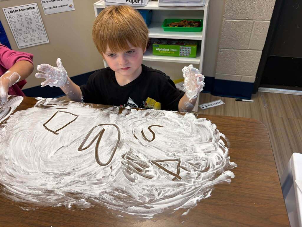 Child writing letters and drawing shapes in shaving cream.