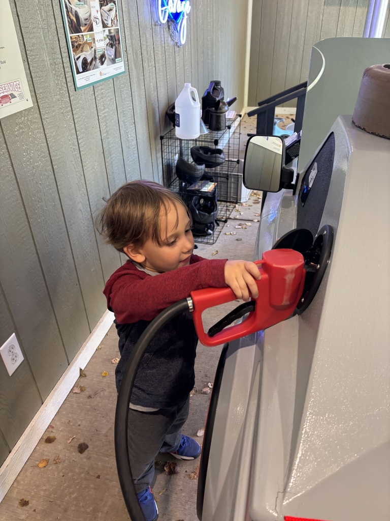 A boy pretends to pump gas in a toy car