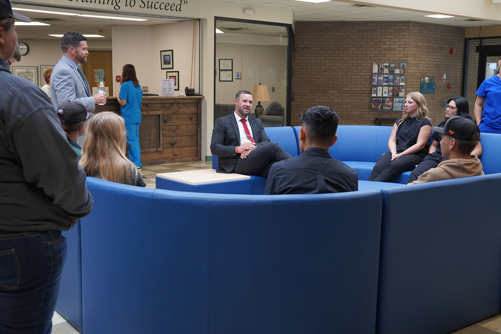 A man sitting on a blue couch talking with several students.