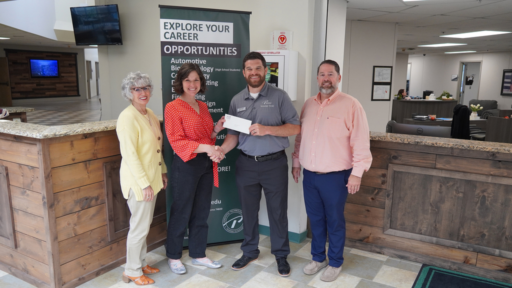 Four people posed with a person in a red shirt giving a person in a grey shirt an envolope