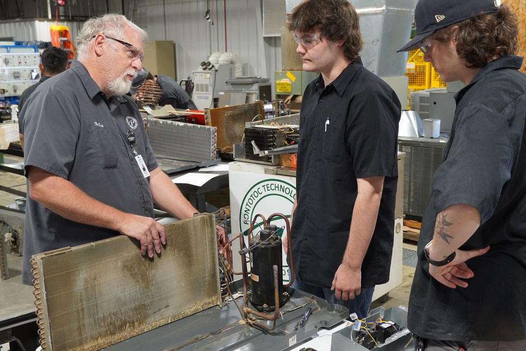 Instructor and student standing next to a workbench with air conditioning parts