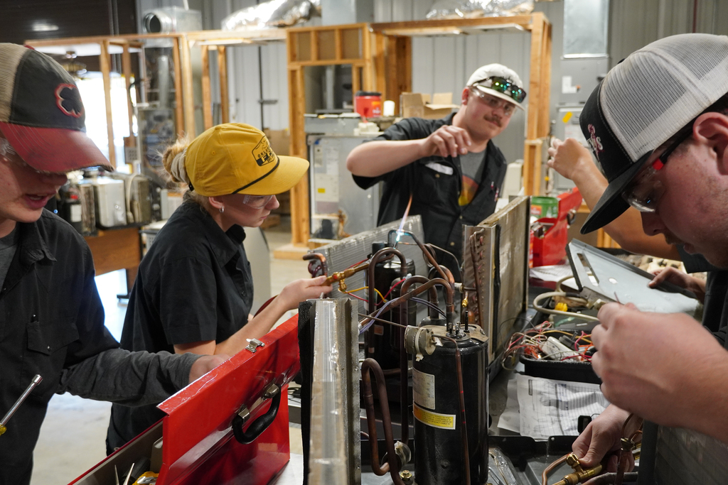 Female student using a torch to connect copper pipe to ac unit