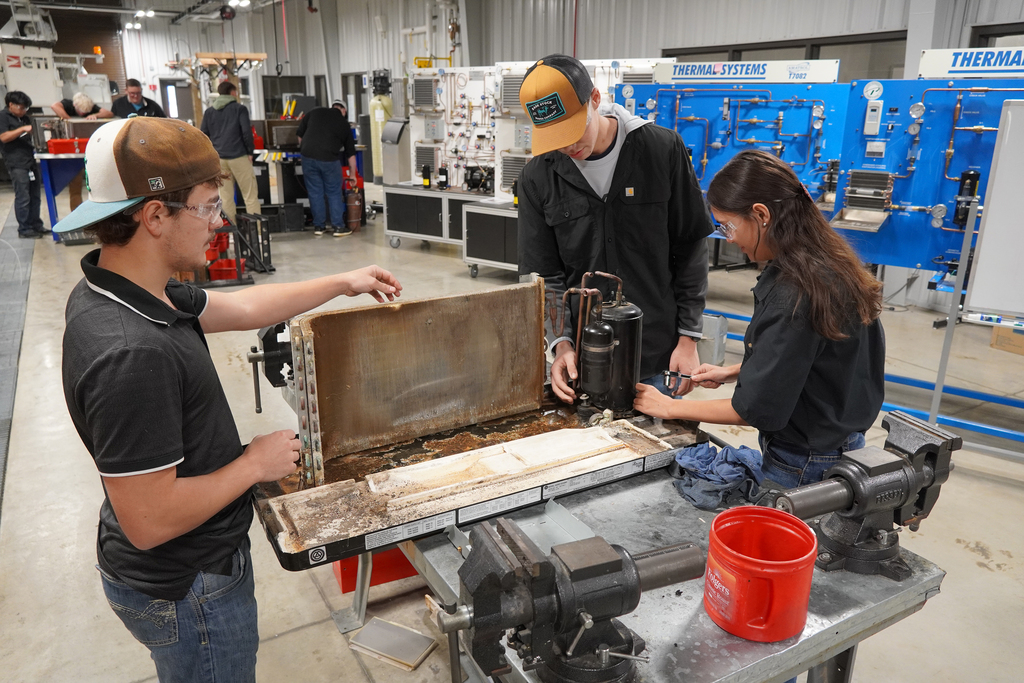 Students removing a compressor from the base of an ac unit