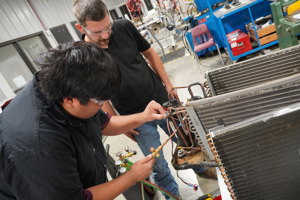 Student watching another student using a torch to connect copper pipe on an ac unit