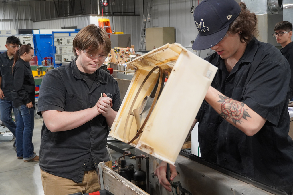 Two students lifting a part out of an ac unit