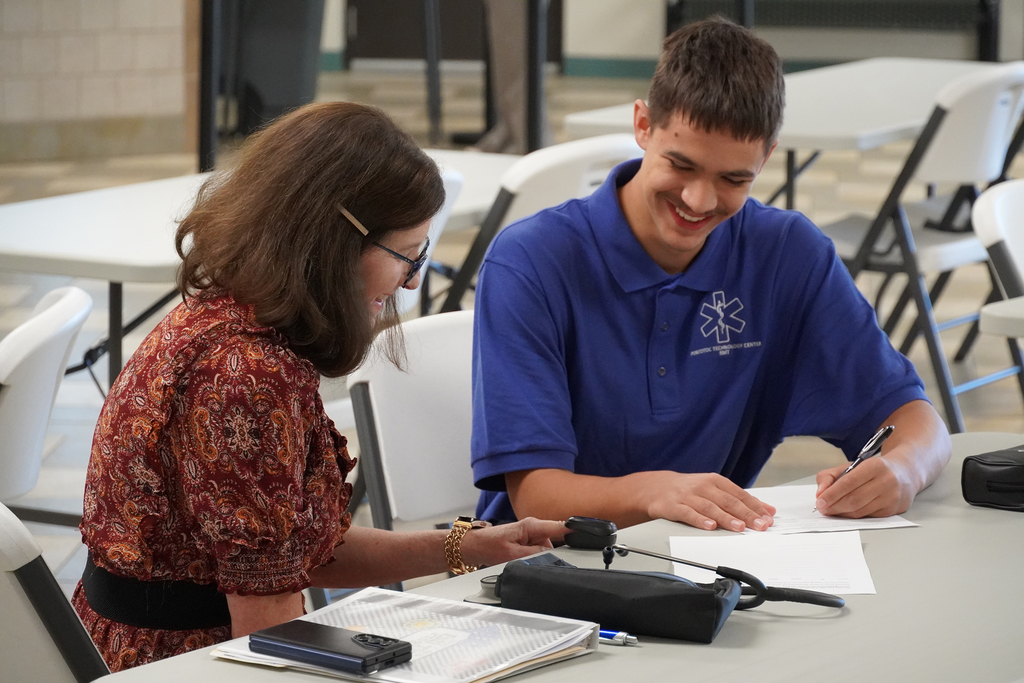 Student sitting with a patient at a table taking a pulse ox reading