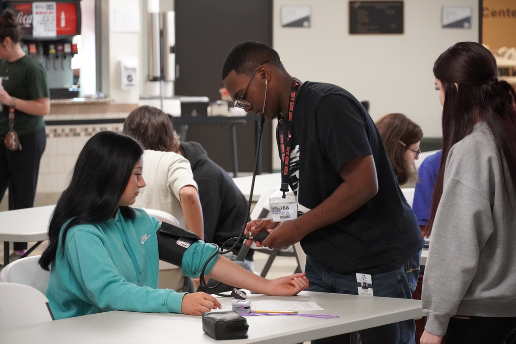 Student standing with patient sitting at a table getting a blood pressure reading