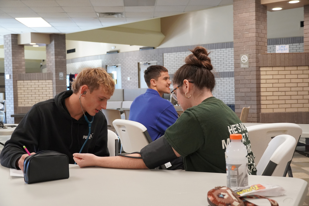 Student sitting with a patient at a table taking a blood pressure reading