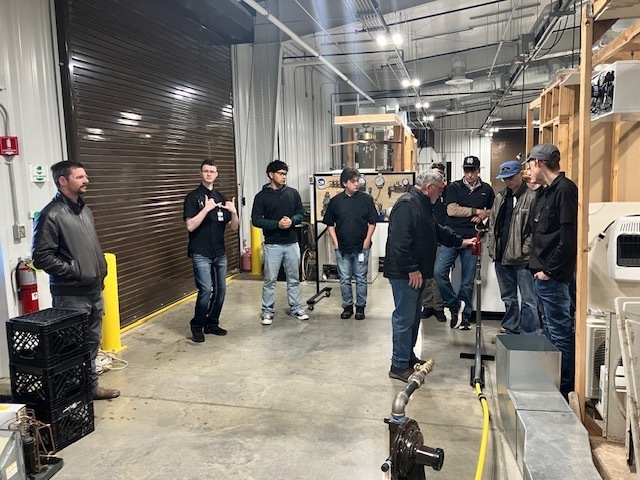People watching a demonstration inside an HVAC training workshop.