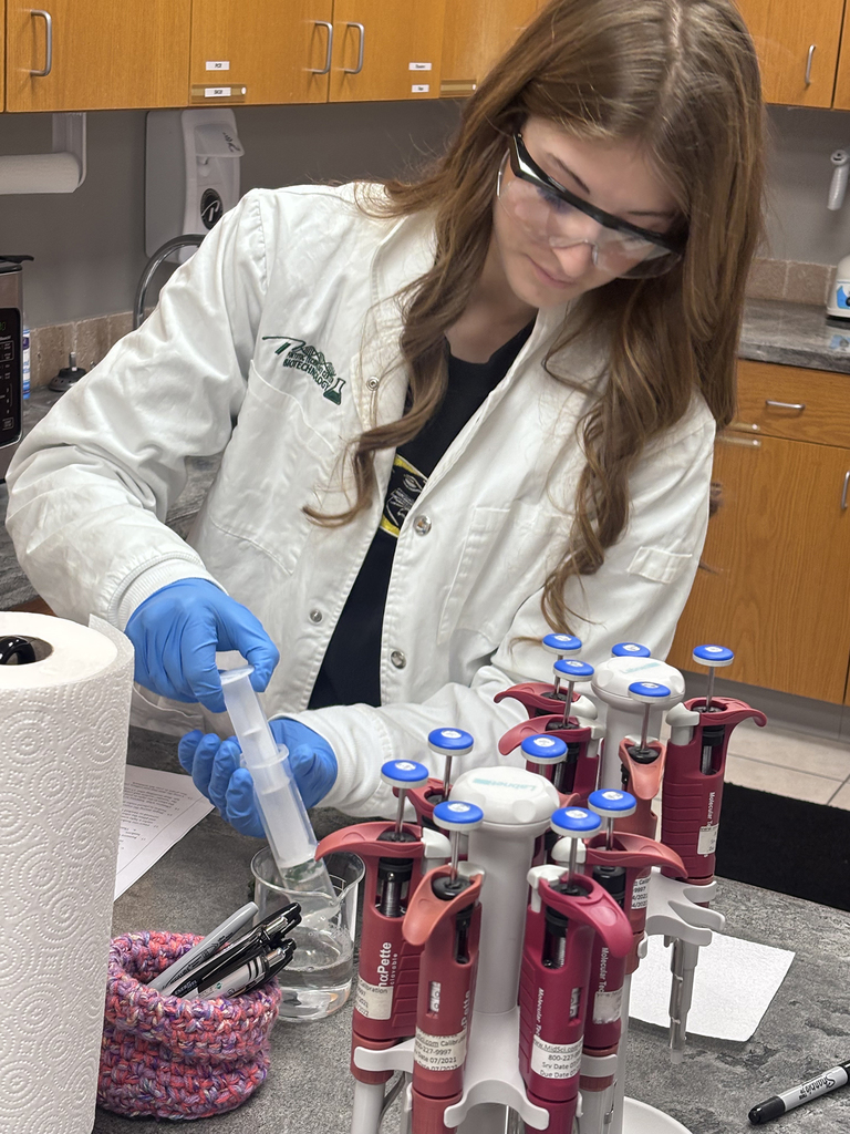 Student in white lab coat preparing a biotech experiment