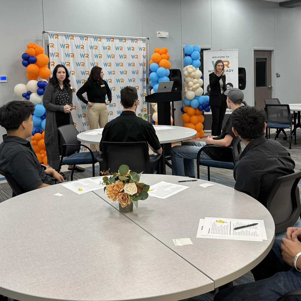 Several people in a classroom setting with presenters at the front of the room.