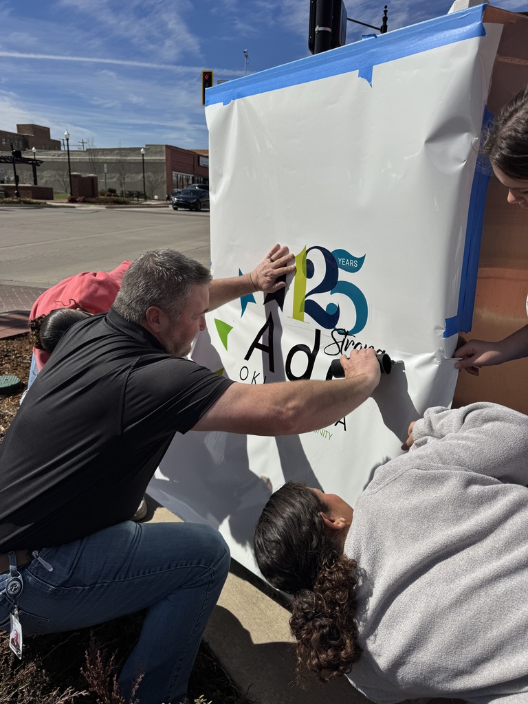 Close up of four people installing a graphic wrap on a large sliver electrical box on a street corner.