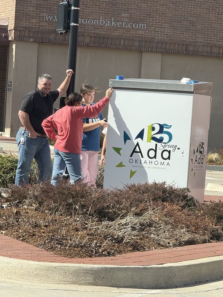 Four people applying graphic wrap to a large silver electrical box next to a street.