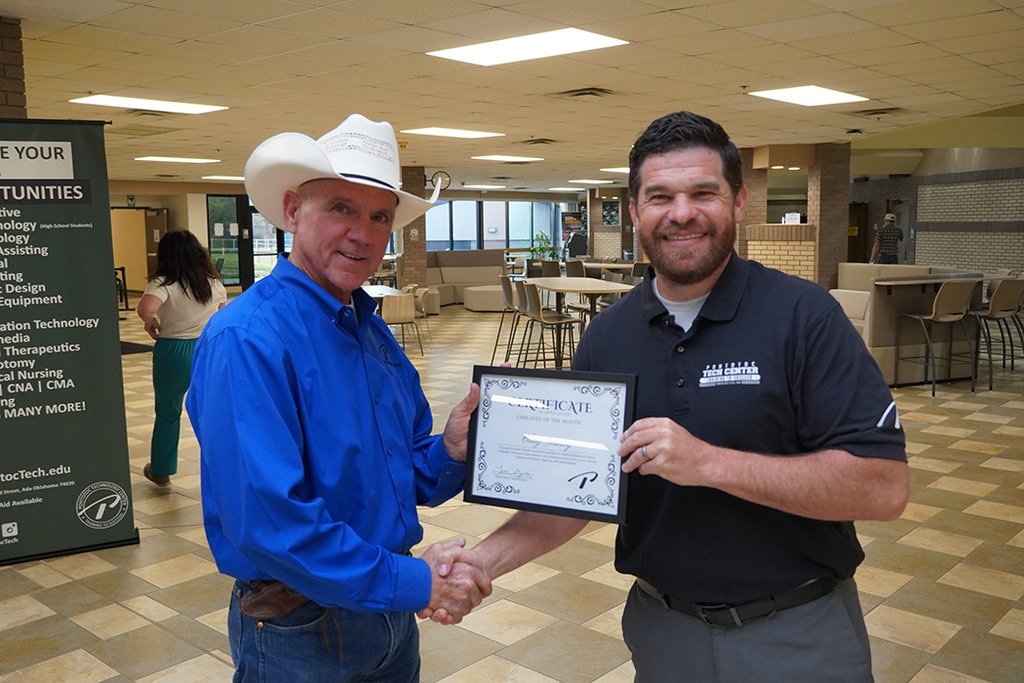 Two people shaking hands exchanging a framed certificate