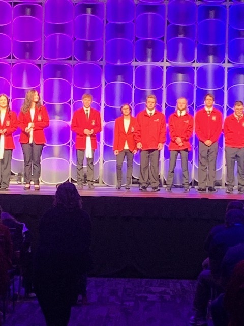 Group of students in red jackets standing on stage.