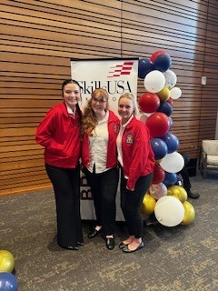 Three students posed in red jackets standing next to baloons.