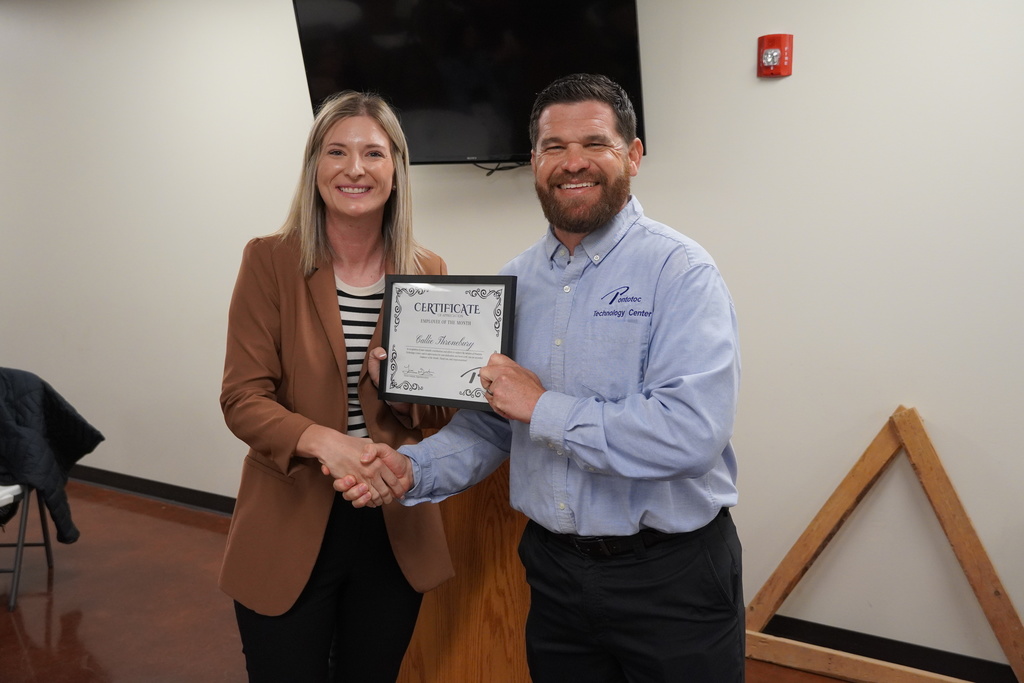 Two people shaking hands and exchanging a framed certificate