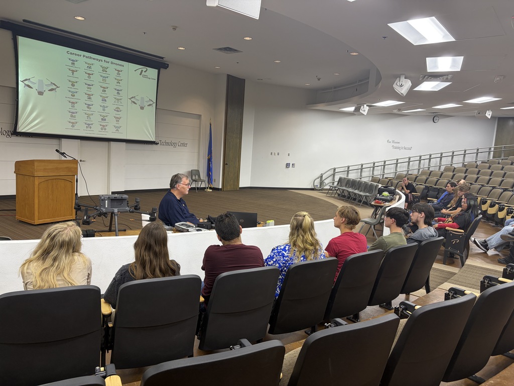 Students in an auditorium watching a presentation with the instructor at front