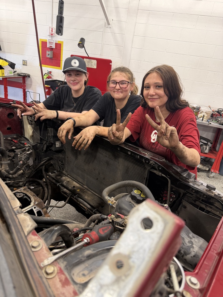 Students posing over an engine smiling at the camera