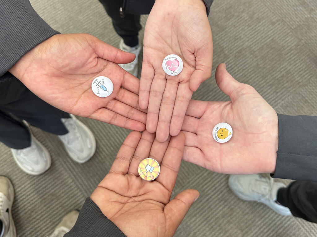 Four hands coming together in the center of the image, holding small buttons in their palms.