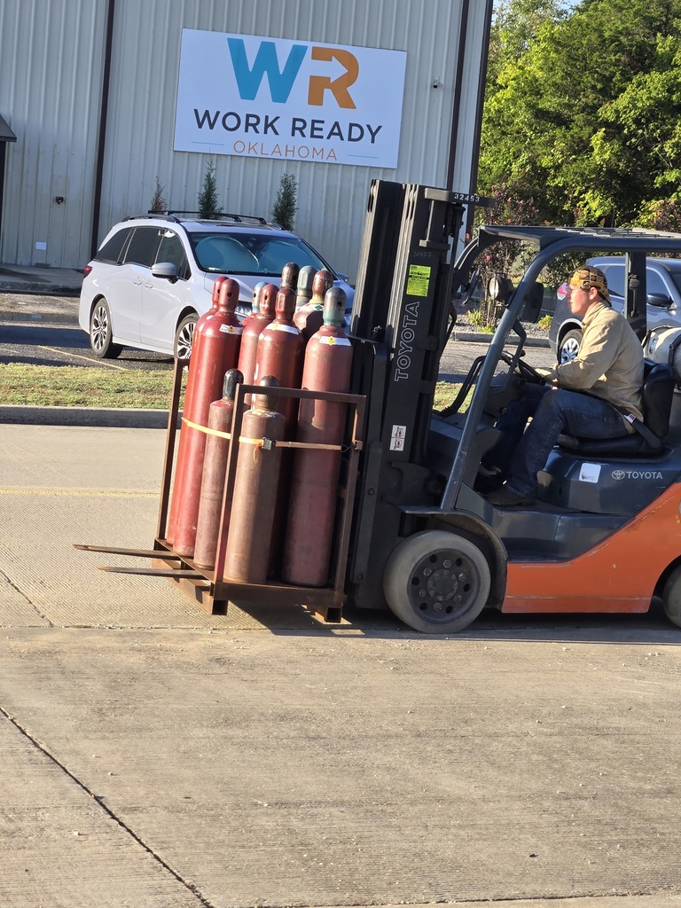 Student operating a forklift to move a rack of gas cylinders