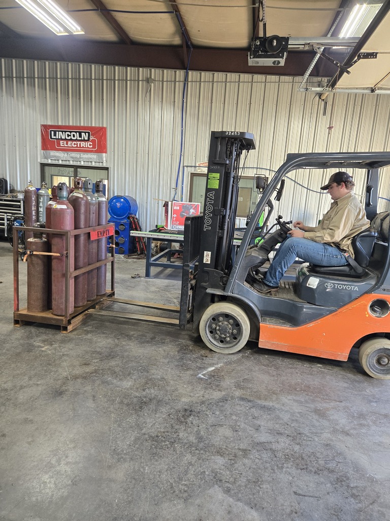 Student operating a forklift to pick up a rack of gas cylinders