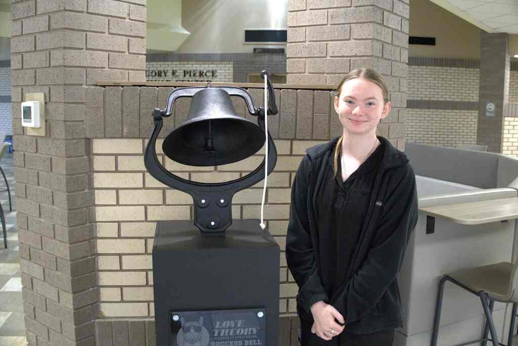 Picture of a female standing next to a bell on a stand