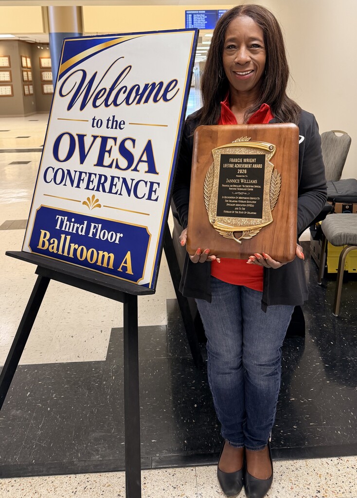 Lady standing holding an award plaque next to a sign on an easel