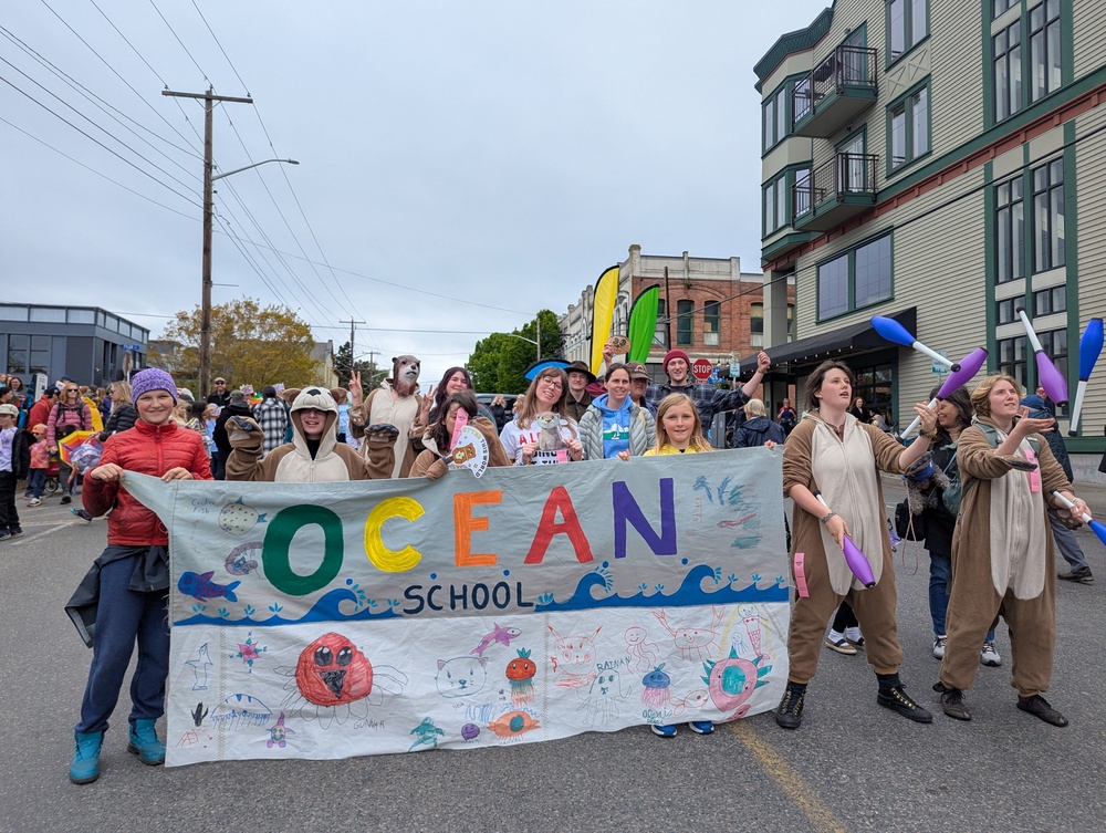 photo of student wearing otter costumes and juggling and holding an OCEAN school banner