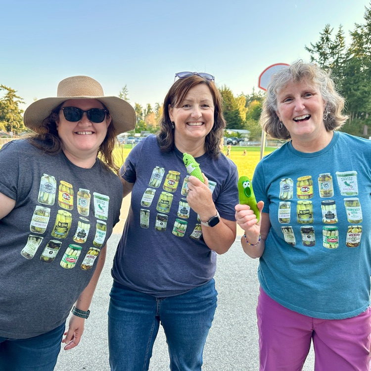 first grade teacher team in matching pickle t shirts smile and hold up fake pickles at back to school night.