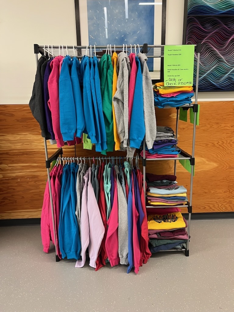 A rack of colorful sweatshirts and t-shirts displayed in the school office showing off the new shipment of Eagle Wear at Salish Coast Elementary.