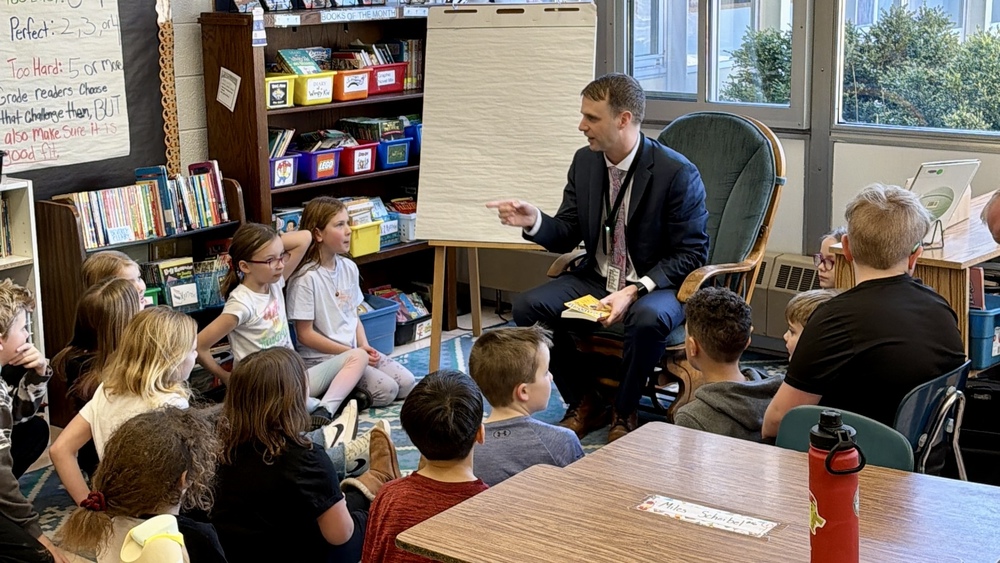 Superintendent reading to a class of kids who are raising their hands