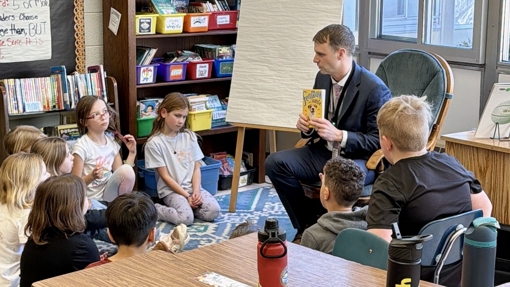 Superintendent reading to a class of kids who are raising their hands