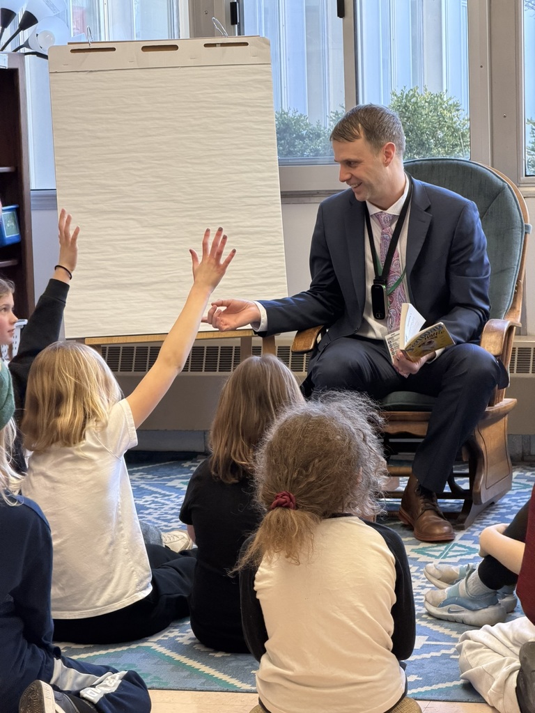 Superintendent reading to a class of kids who are raising their hands