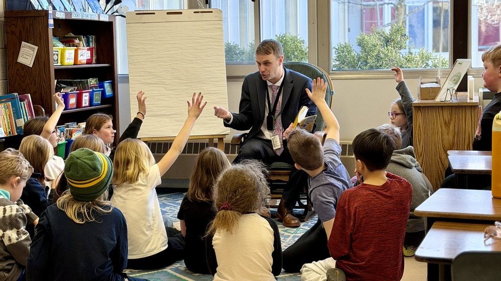 Superintendent reading to a class of kids who are raising their hands