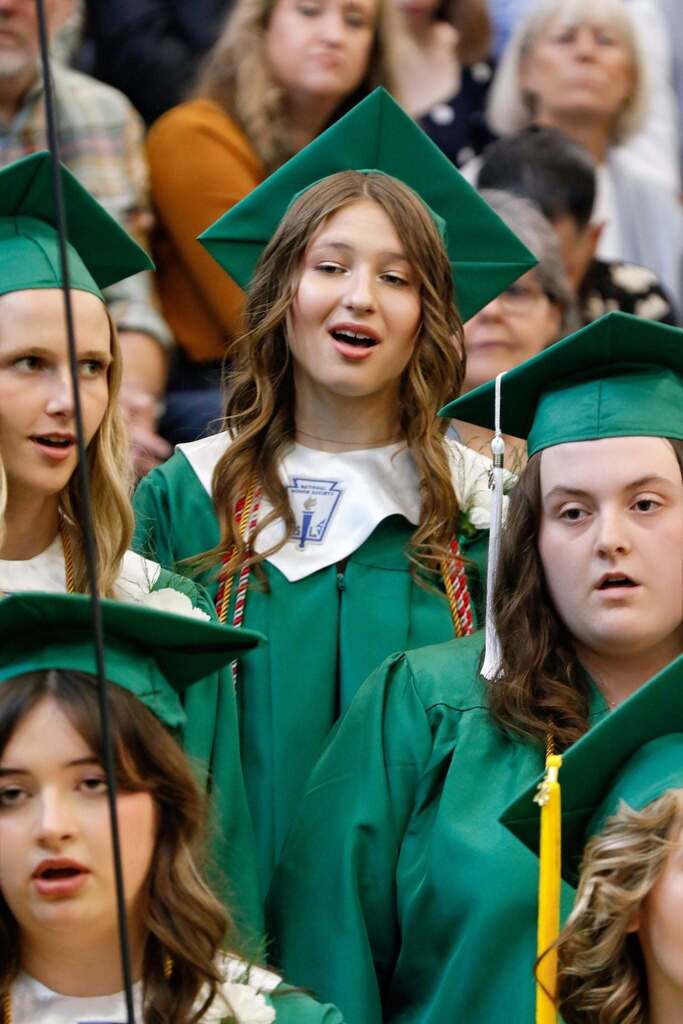 one student in graduation clothing singing as a part of a choir