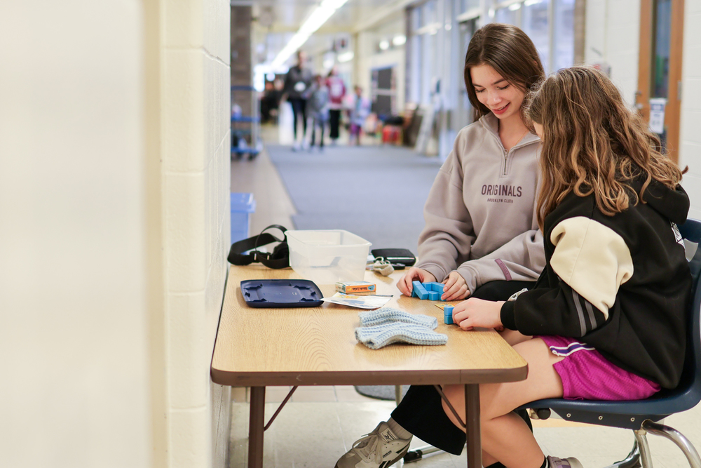 a high school girl sitting with an elementary student at a desk
