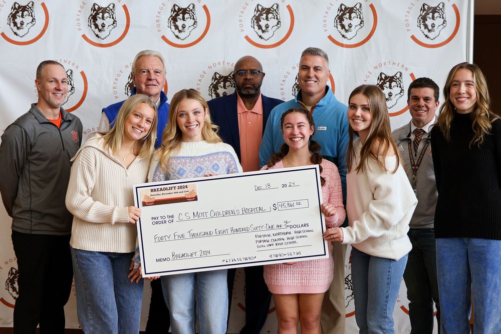 a group of students and adults pose for a photo with a check