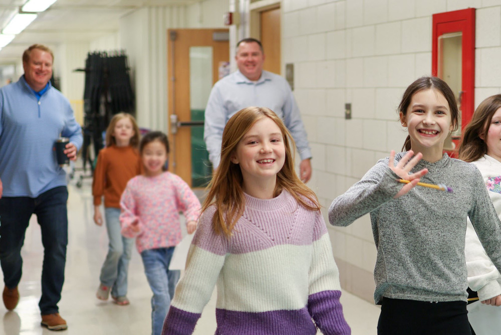 girls smile for a photo while walking down a school hallway