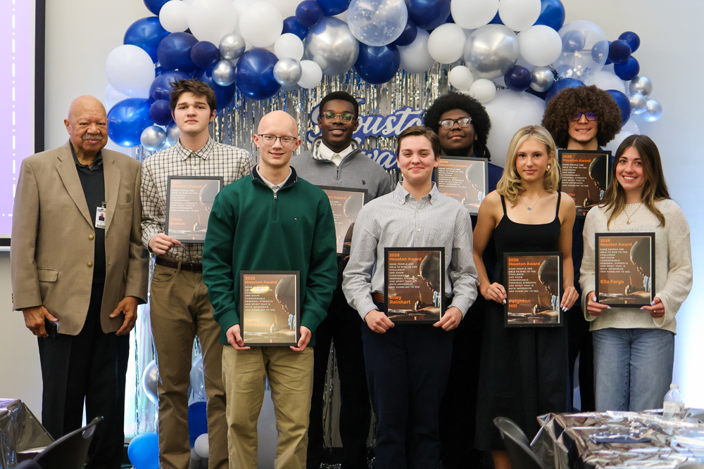 a group of students pose for a photo holding plaques in front of blue balloons