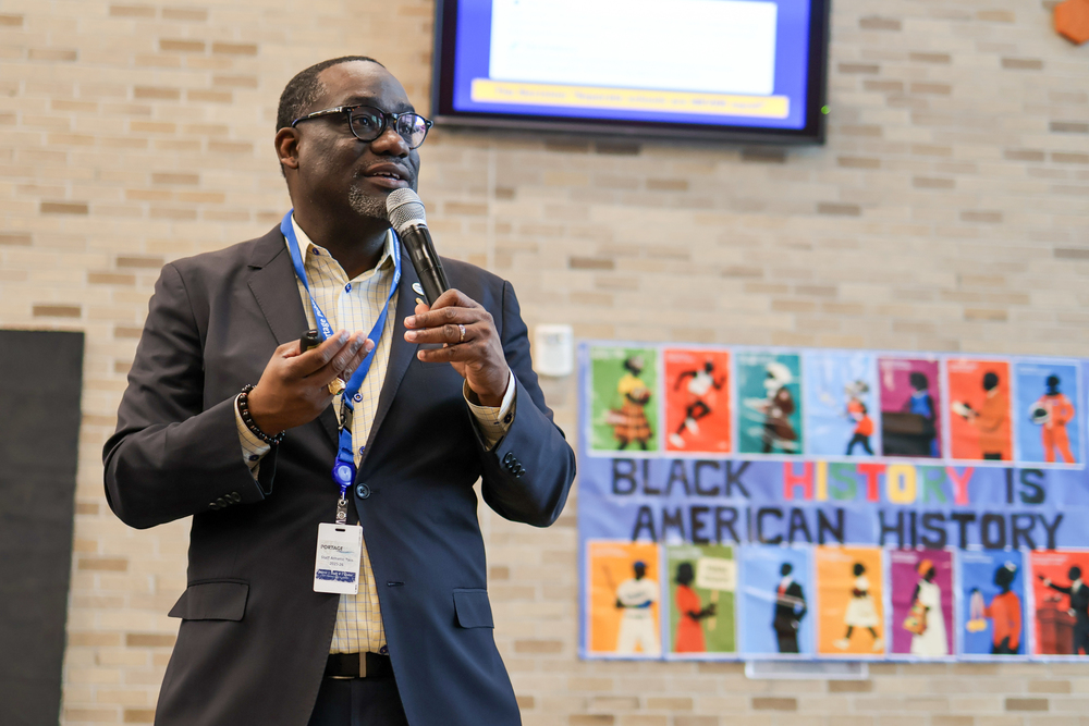 a man speaking in front of a sign that says black history is american history