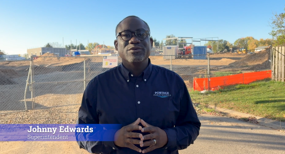 a man talking to the camera in front of a construction zone