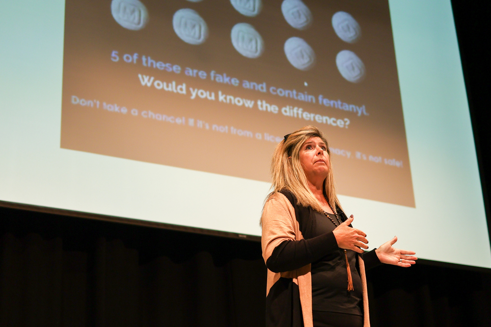 a woman speaking on stage in front of a screen that talks about fentanyl