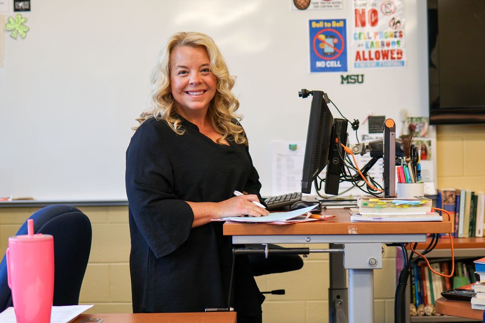 a woman stands at a desk in a classroom