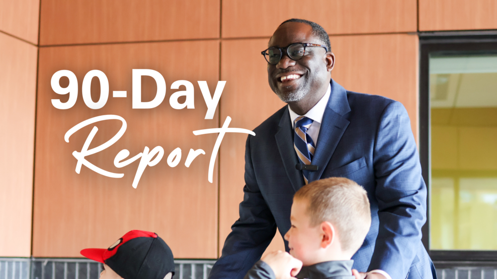 a man smiles outside a school. words say 90-day report