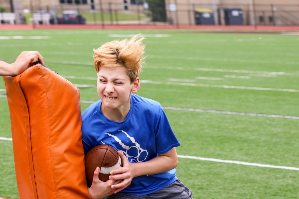 a boy carrying a football collides with a blocker on a football field