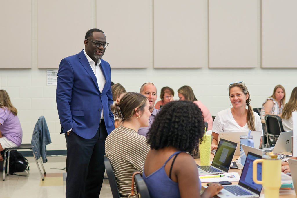 a man stands and talks to people sitting at tables in a room
